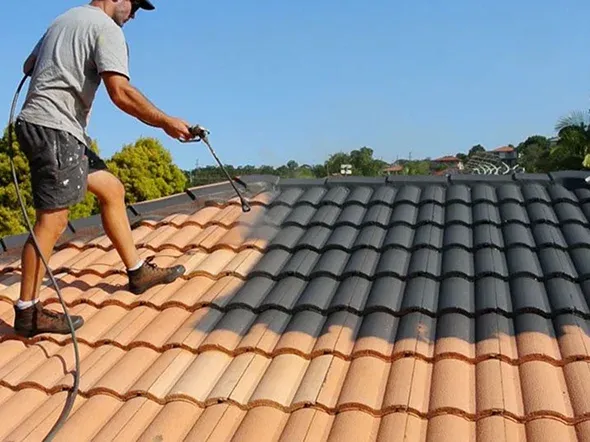 Man spraying paint on a tiled roof